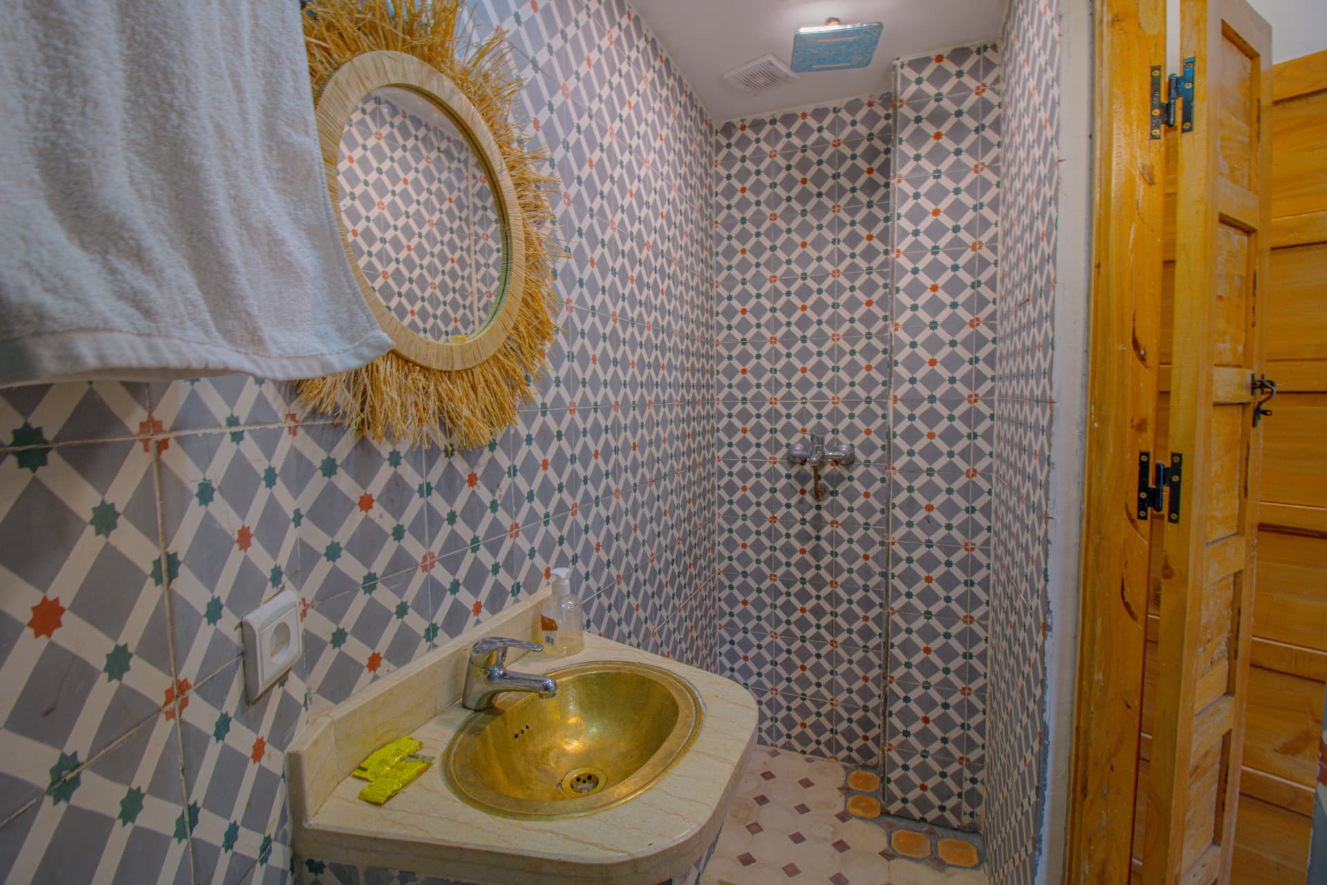 SAGHRO — bathroom in grey star zellige with brass basin and raffia mirror