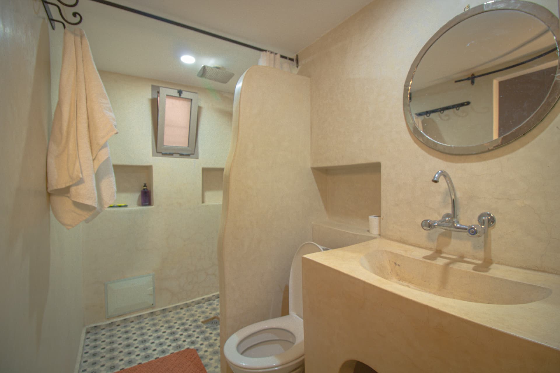 ANYA — tadelakt bathroom with round mirror and walk-in rain shower