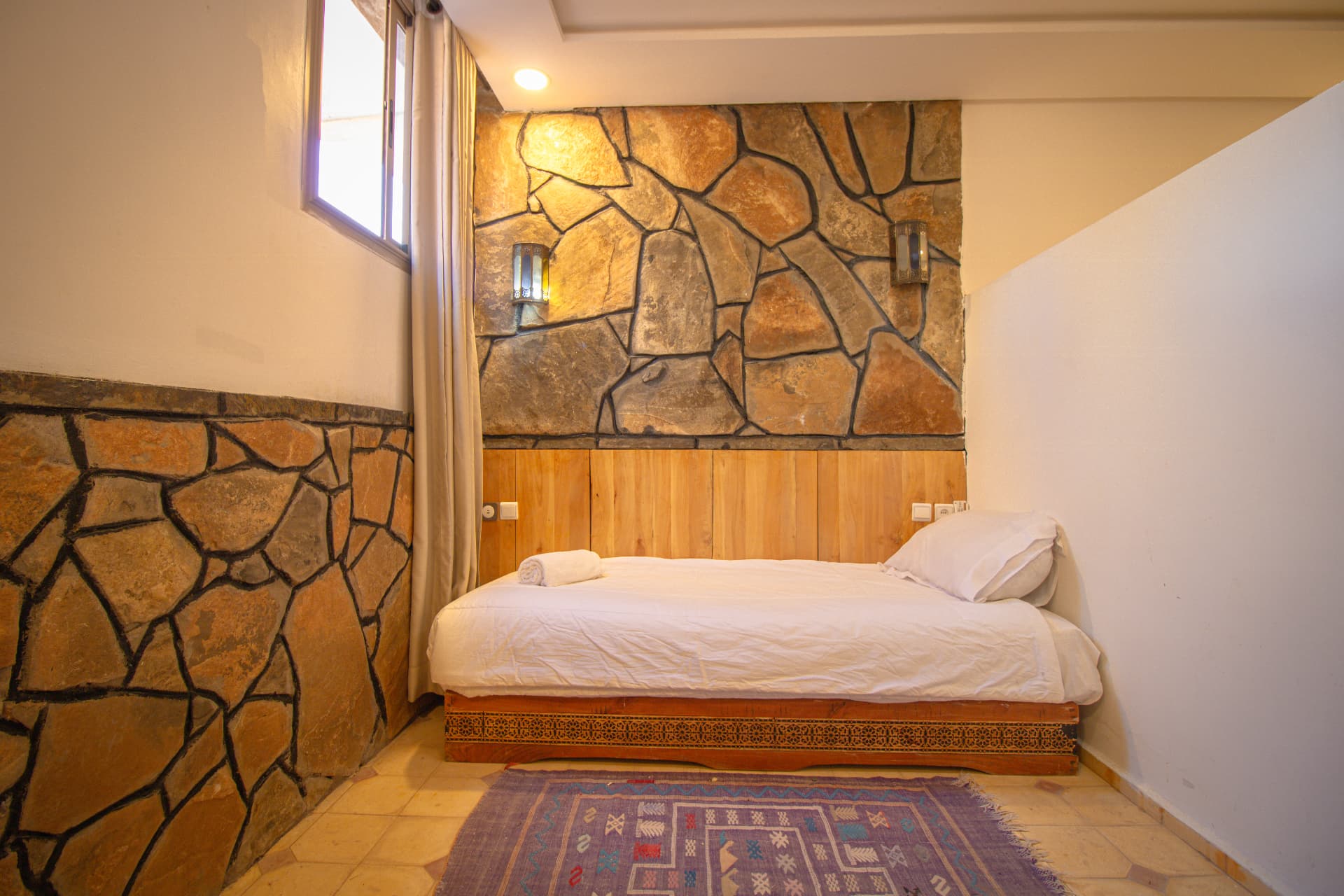 TAZDYI — single bed alcove with carved wooden base, stone wall and window light