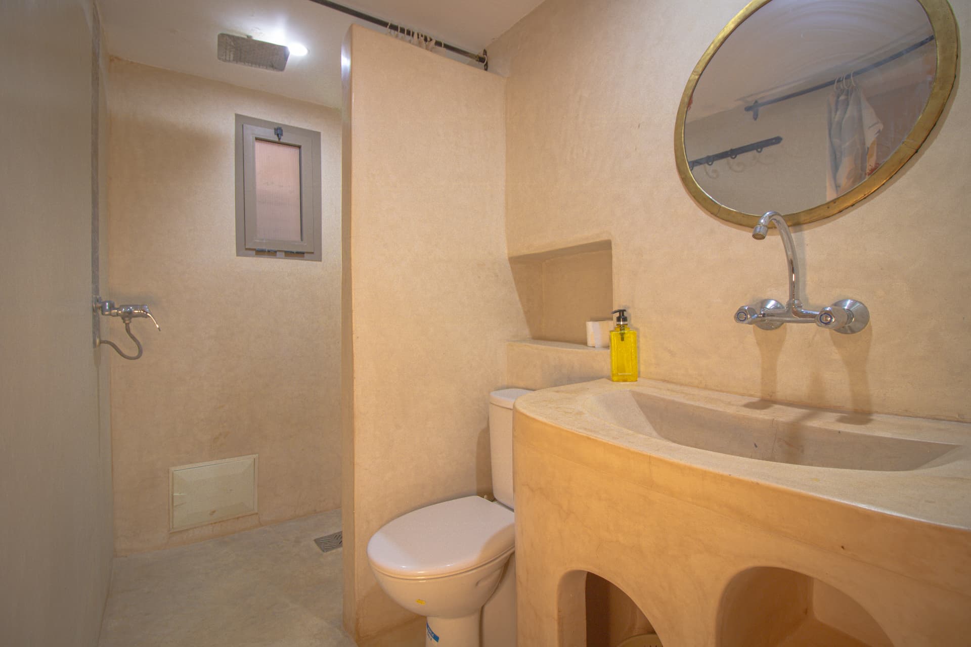 AFRI — tadelakt bathroom with round brass mirror and walk-in shower