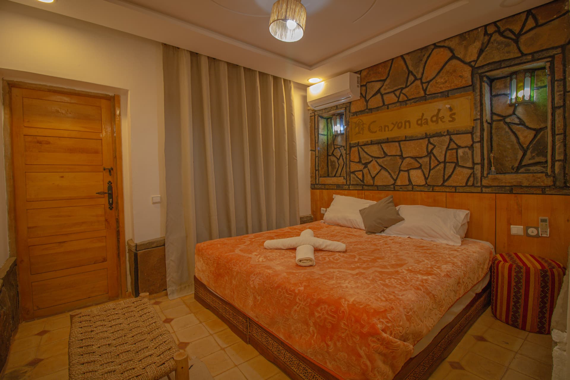 ZIZ — wide view of the room with stone feature wall, double bed, wooden door and woven bench