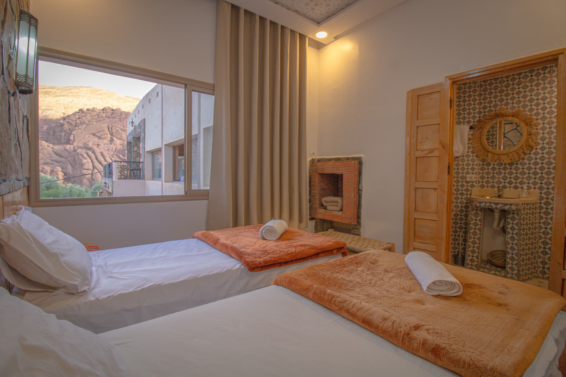 SAGHRO — twin beds beside the window framing the canyon rock and the zellige bathroom