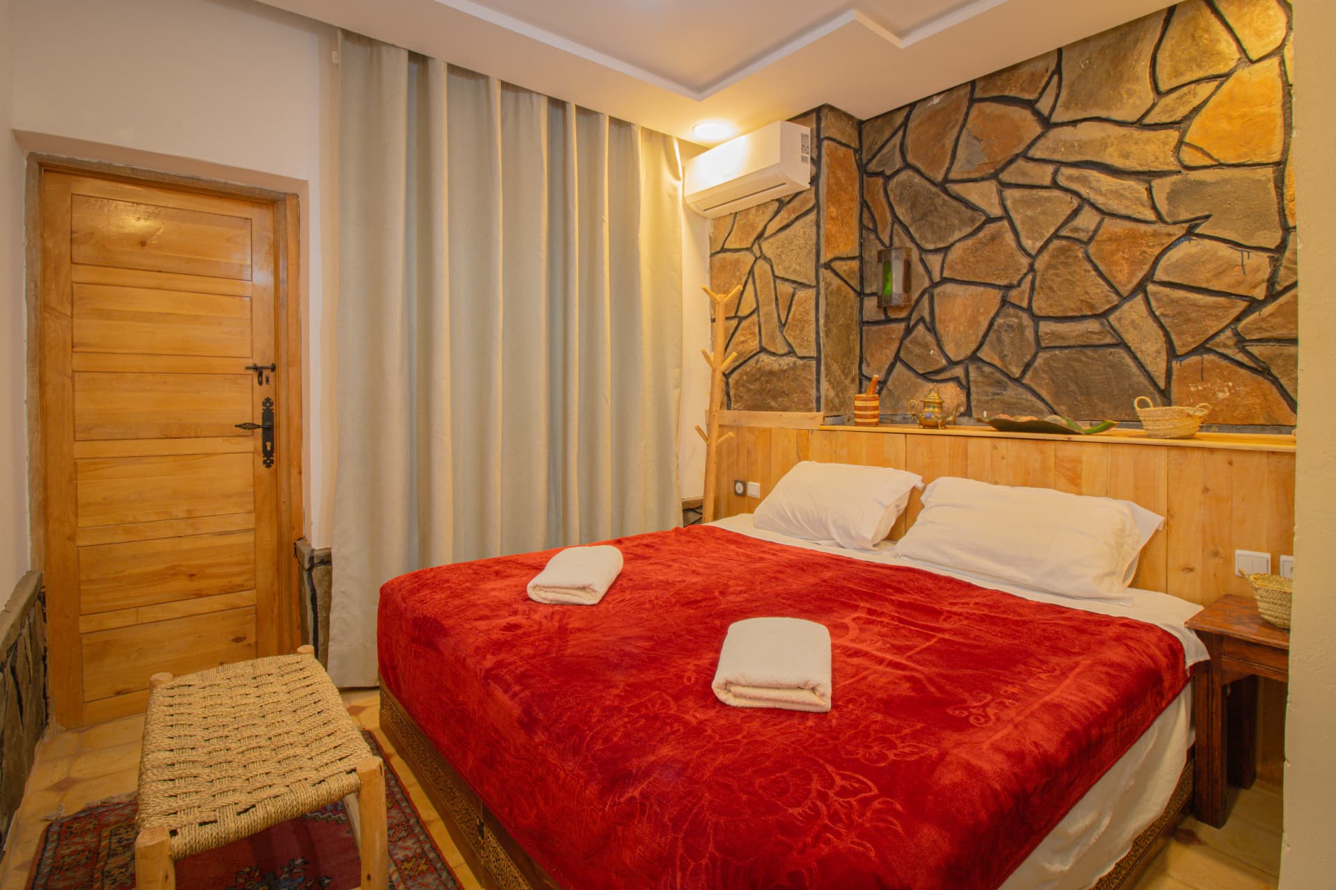 DRAA — wide view of the room with stone feature wall, double bed, woven bench and wooden door